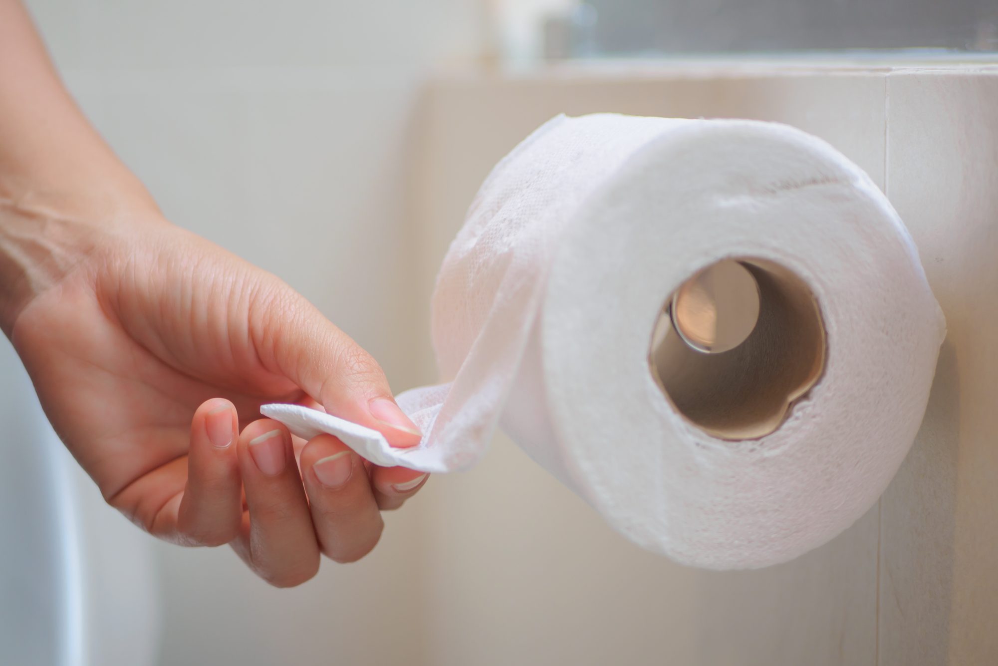 Closeup female hand picking a white tissue from tissue roll in the restroom.