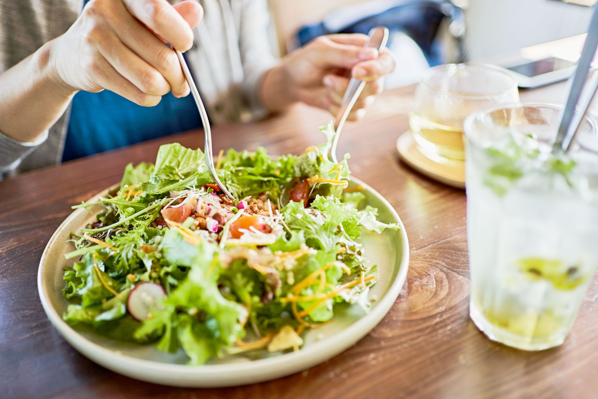 close up of hands with utensils eating a salad