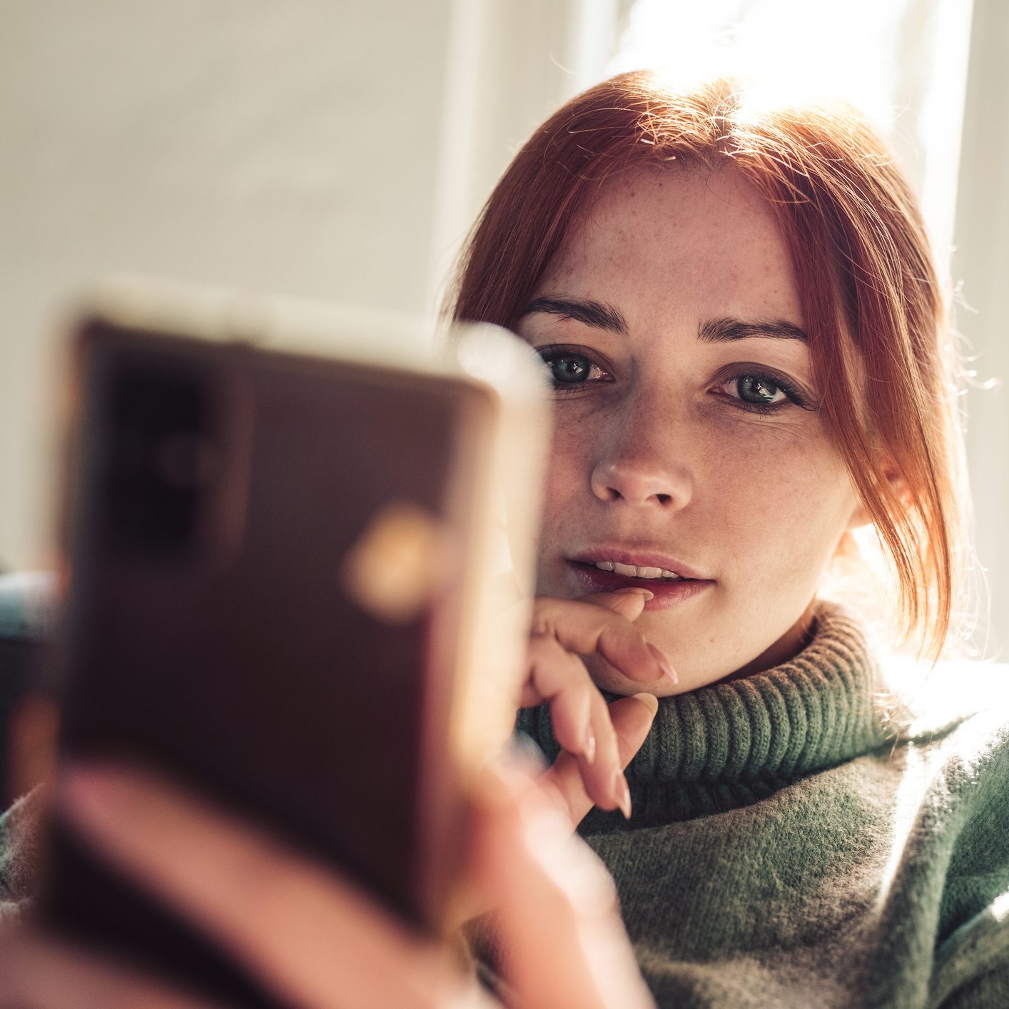 Woman with red hair looking on screen of her mobile phone.