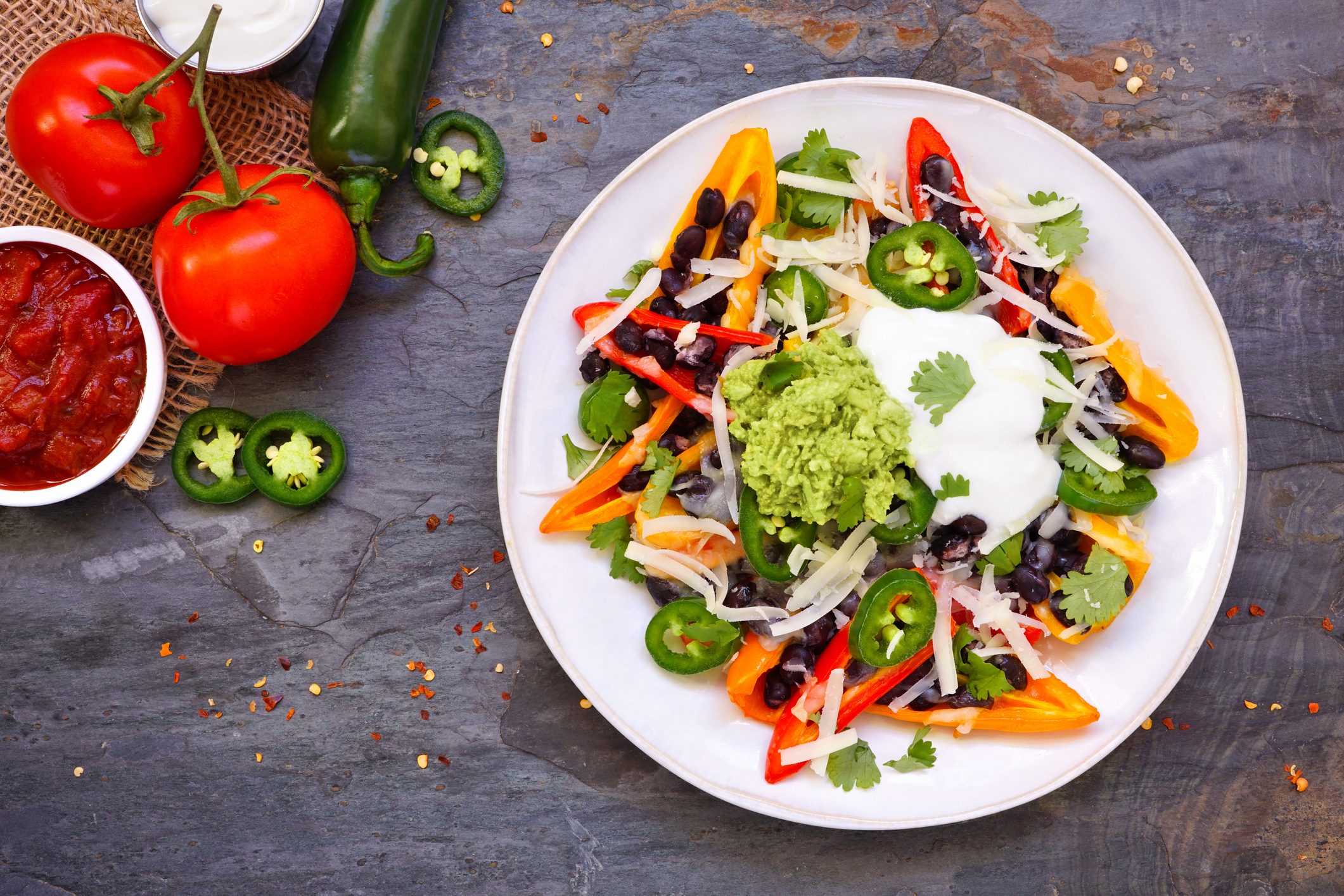 Healthy, plant based bell pepper nachos. Above view table scene on a dark background.