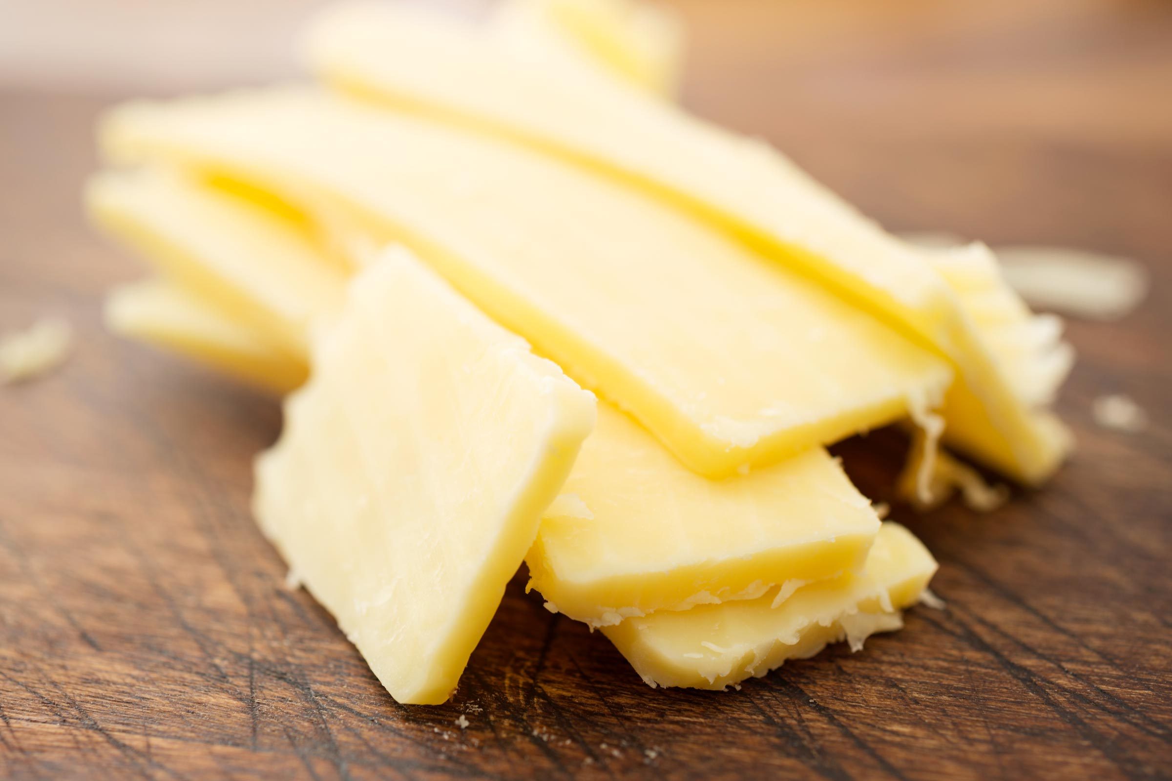 Slices of cheddar cheese on a worn rustic chopping board.