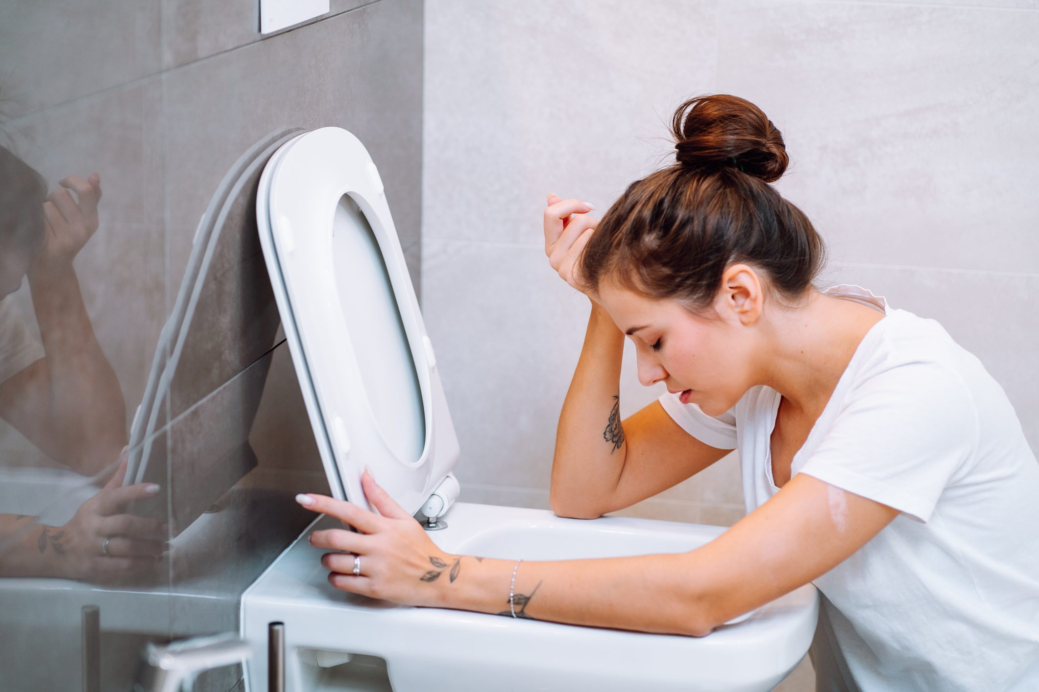 Young woman feeling sick, throwing up, vomiting in toilet