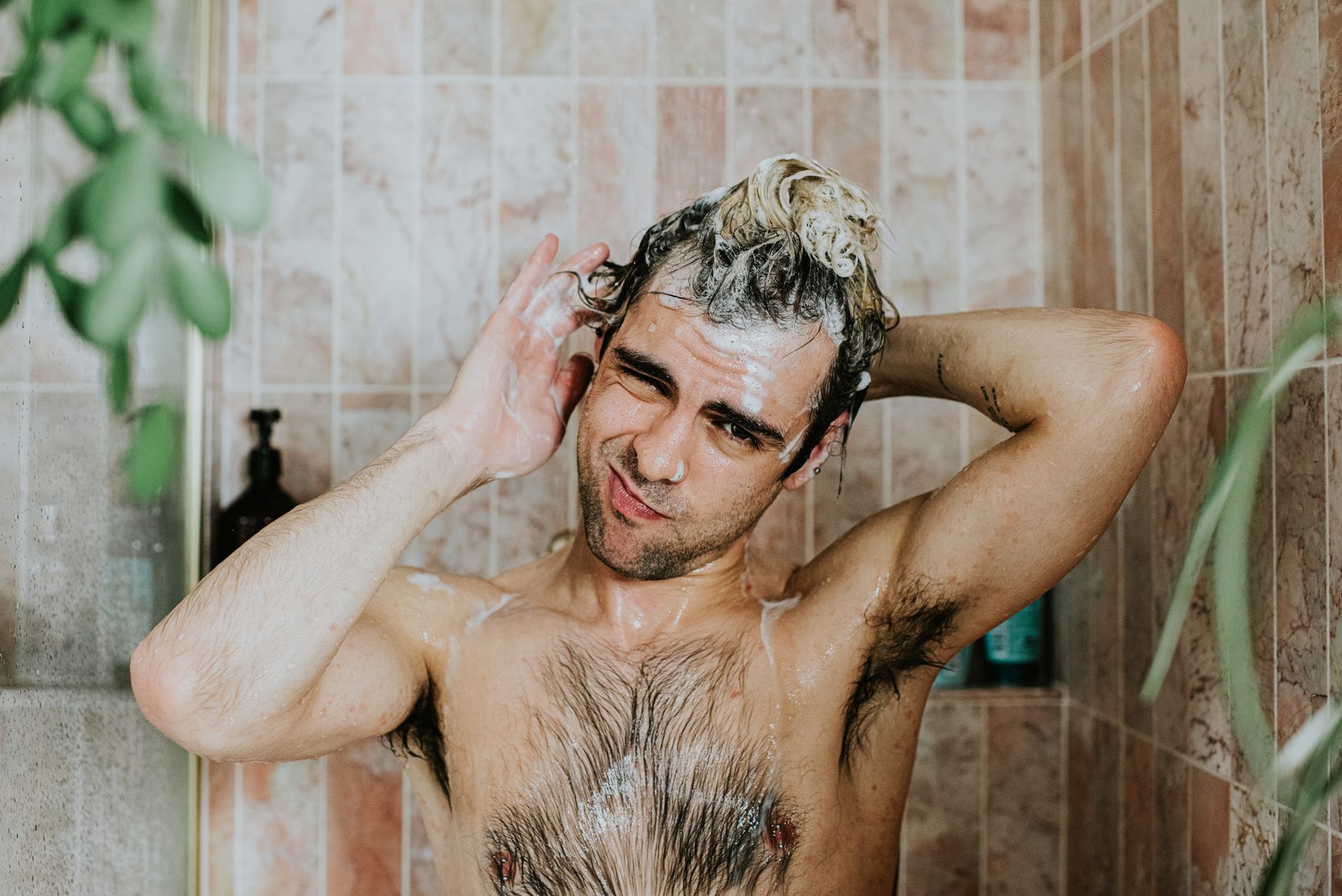 Portrait of a man washing his hair in the shower. He looks at the camera.