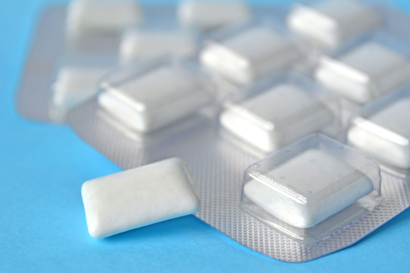 close up of a pack of white gum on blue background. one piece is outside the pack in the foreground