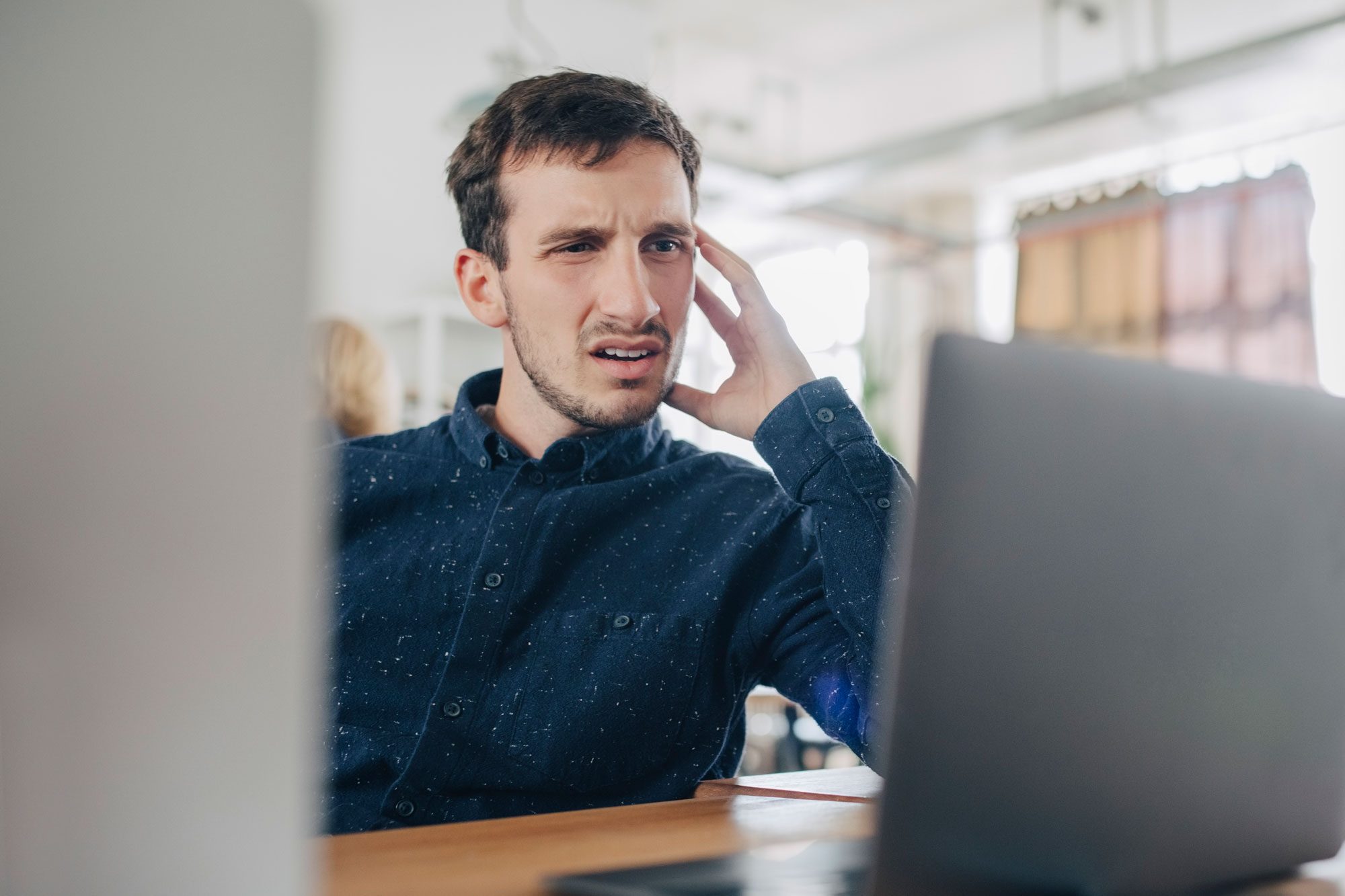 Confused Businessman Looking At Laptop While Sitting At Desk In Office