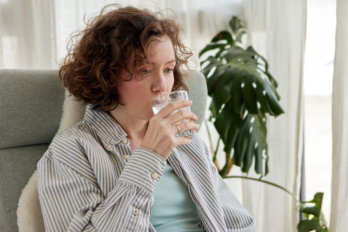 Curly Woman Drinks Water From A Glass