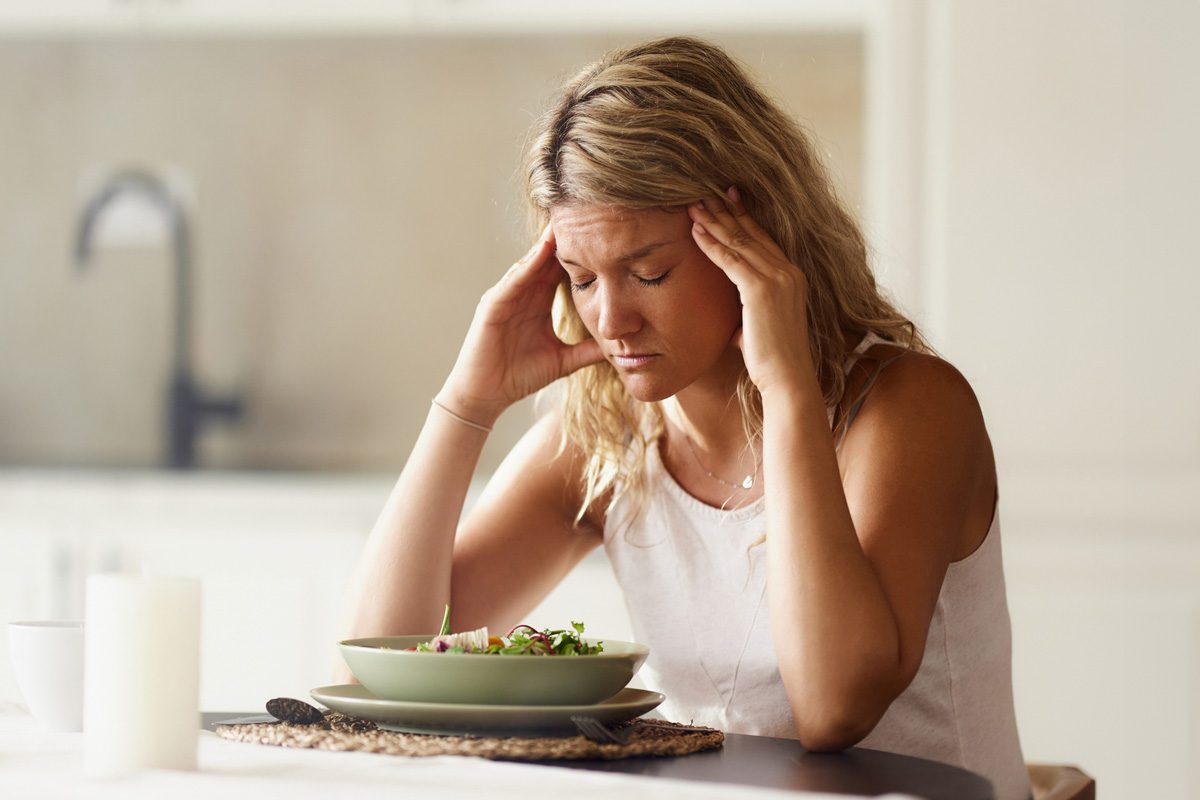 woman holding her head in pain during breakfast at dining table